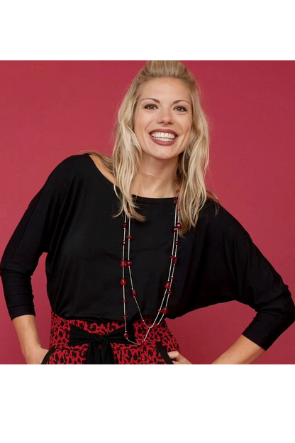 Waist up view of a woman wearing the Jo Slouch Tee by Mandala in Black, standing  in front of a red background 