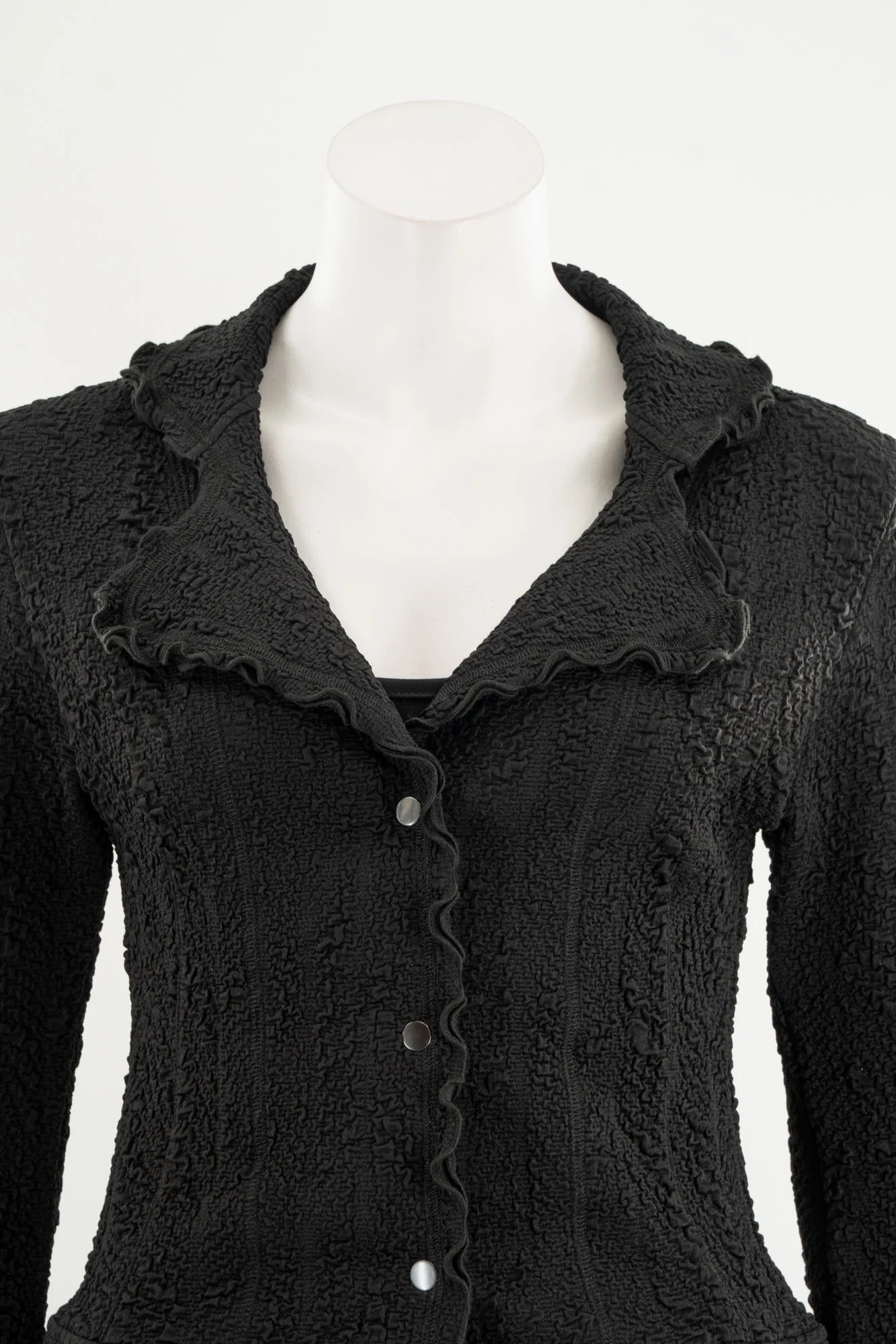 The Essential Jacket - Jasper by Karkass is shown on a mannequin in front of a white background. It's a black textured jacket with a ruffled collar, button closure, and frill details at the cuffs and hem. 