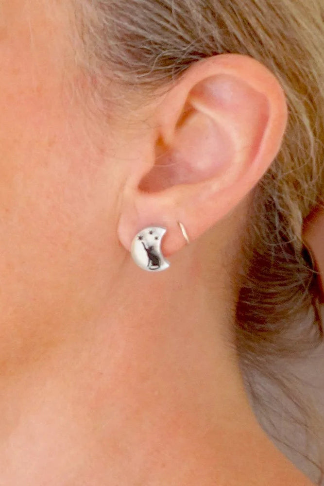 Close-up of a person wearing a silver moon shaped earring with a black cat design. 