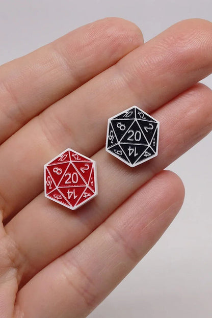 Two Lilipop DND dice earrings,  one red and one black, held between fingers against a neutral background.