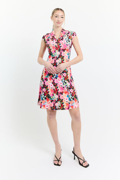 A woman wearing the Sky Dress by Dinh Ba in Pink print, an A-line floral dress with a cowl neck, cap sleeves, and above the knee hem. She is standing in front of a white background. 