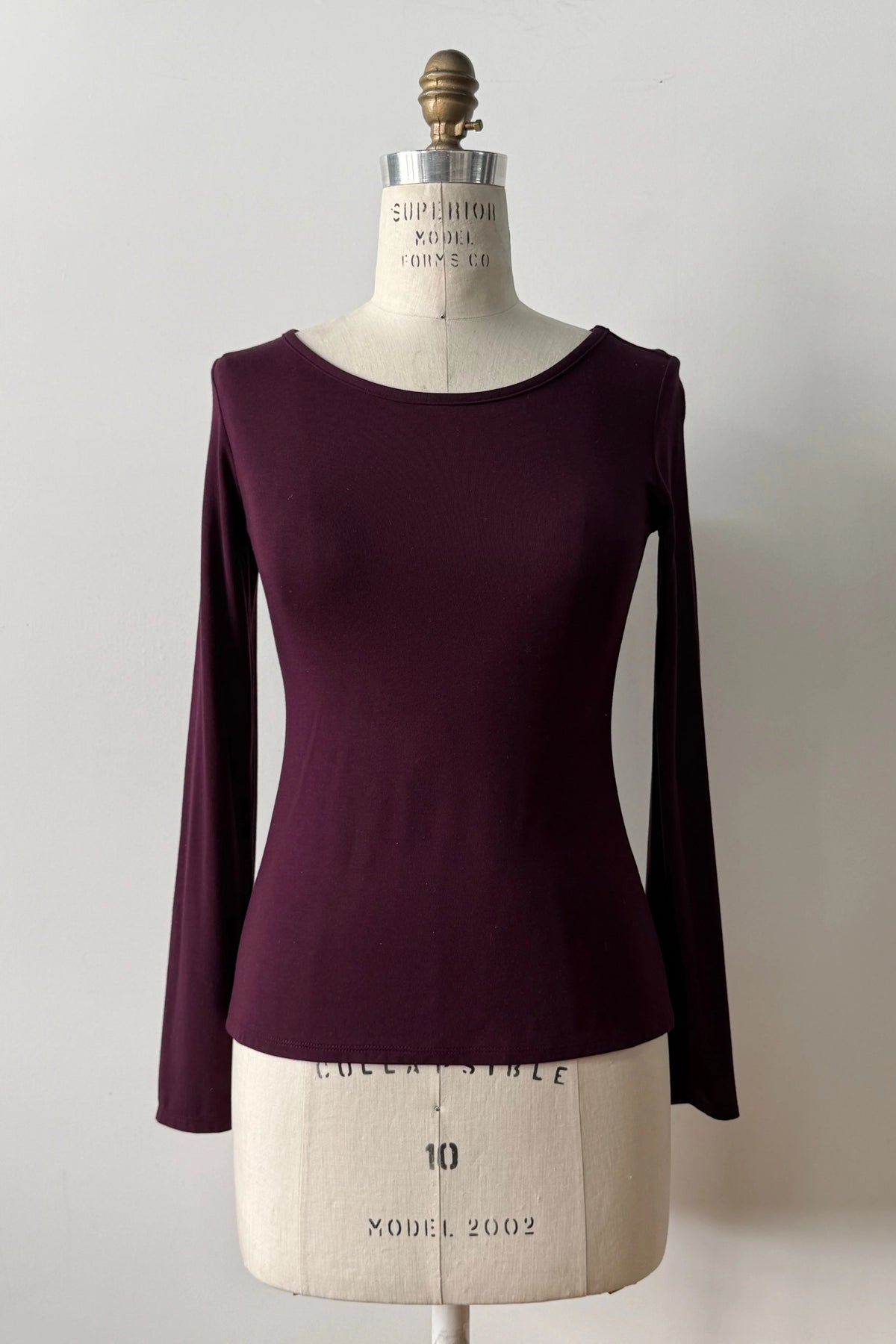 The Loretto Top by Kollontai in Burgundy, a slim fitting long sleeved top with a round neck, is shown on a mannequin against a white background. 