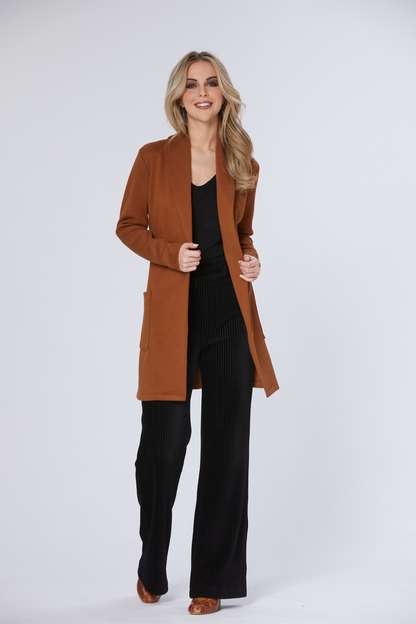 A woman wearing the Dop Cardigan by Luc Fontaine in Caramel with Black pants, standing in front of a white background 