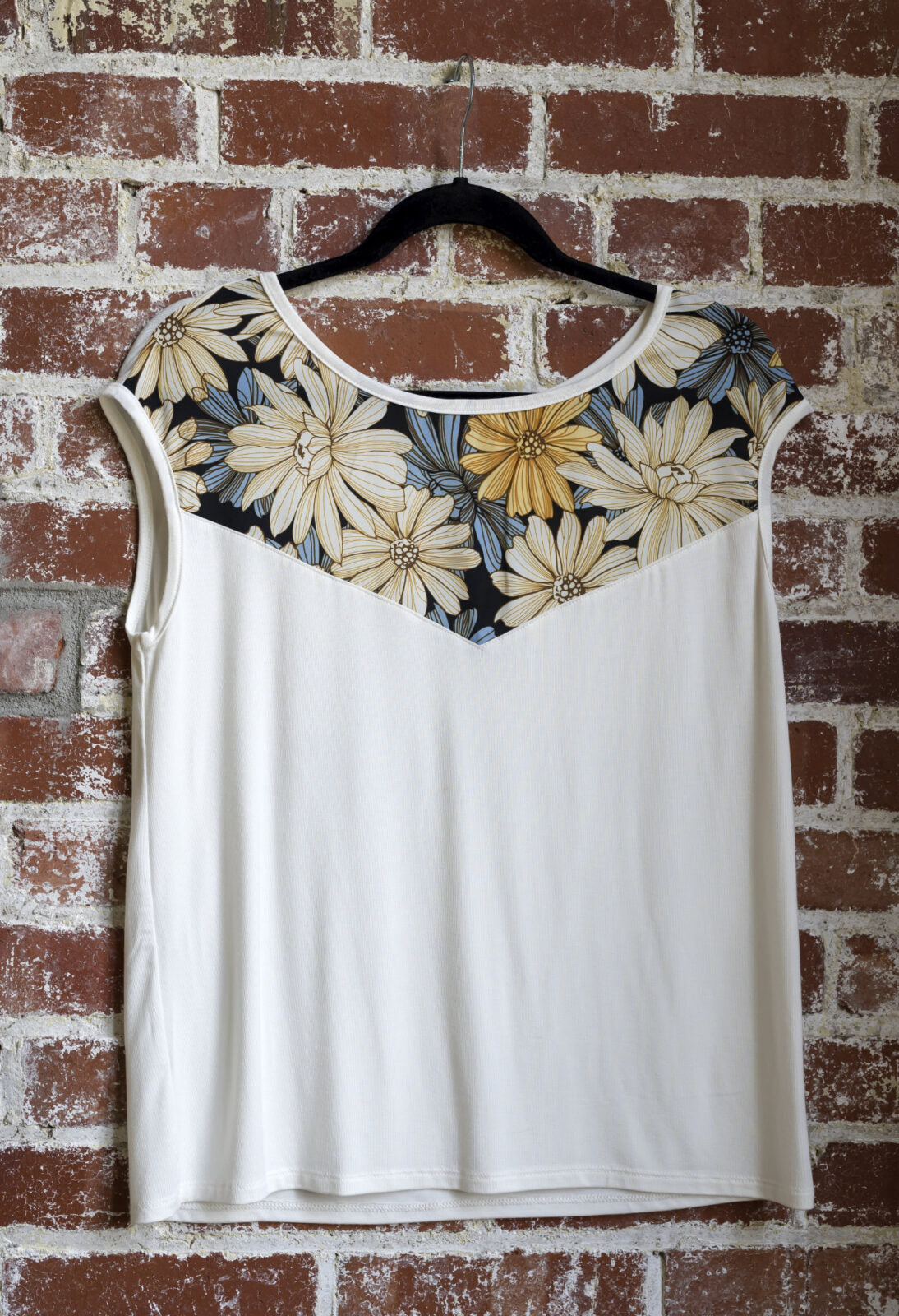 The Marie C Pepita Reversible Top in Ivory is shown hanging against a brick wall. The cap-sleeved top features patterned fabric across the chest on one side with solid colour on the other side. 