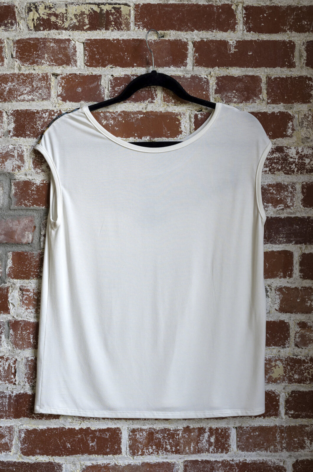 The Marie C Pepita Reversible Top in Ivory is shown hanging against a brick wall. The cap-sleeved top features patterned fabric across the chest on one side with solid colour on the other side. 