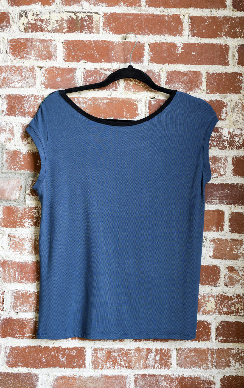 The Marie C Pepita Reversible Top in Blue is shown hanging against a brick wall. The cap-sleeved top features patterned fabric across the chest on one side with solid colour on the other side. 