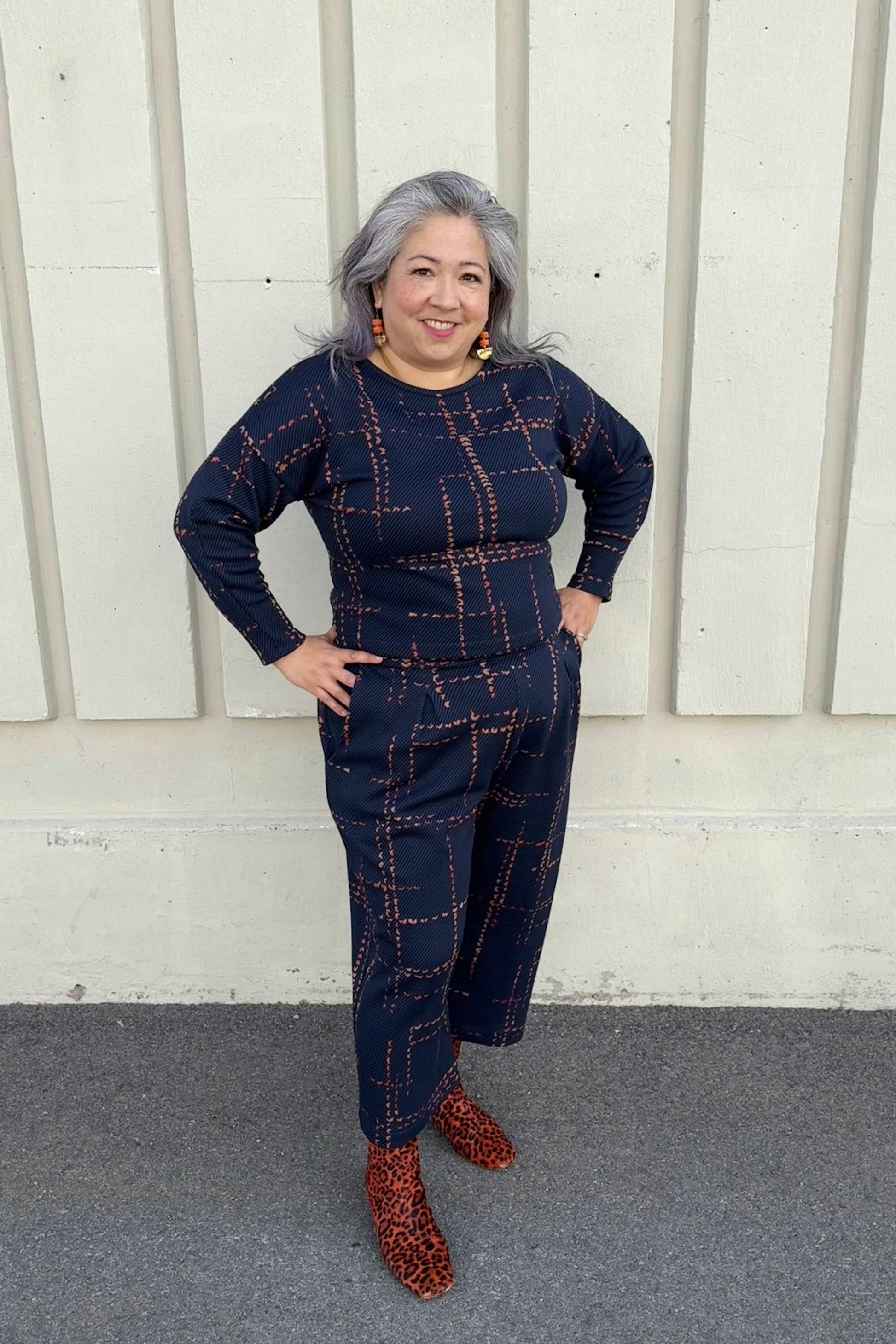 A woman wearing the Jackson Top and Julian Pants by Melow in Indigo, standing outside in front of a white wall