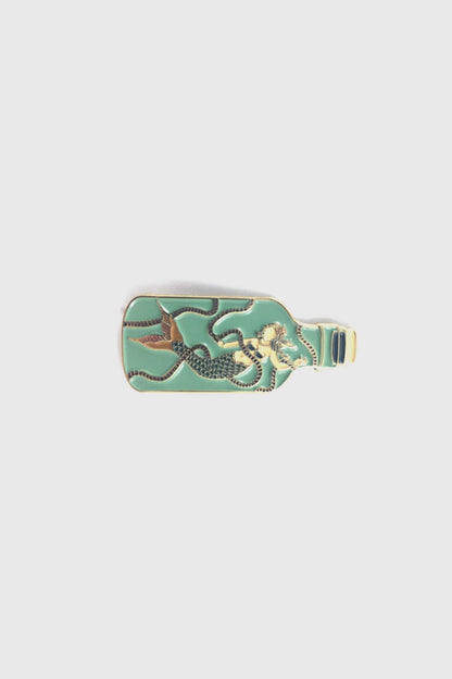 The Mermaid in a Bottle Pin from Badaboöm Studio, an enamel pin featuring a mermaid trapped in a light green bottle, is shown against a white background. 