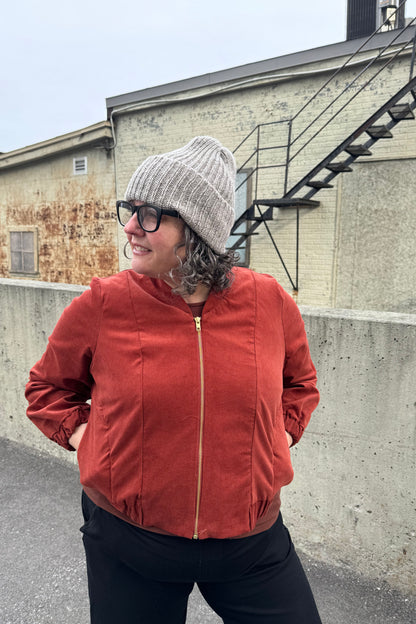 A woman wearing the Ribbed Beanie by Charlevoix Pure Laine in Grey. She is wearing it with the Redrawn Zip Jacket by Eve Lavoie and is standing outside. 