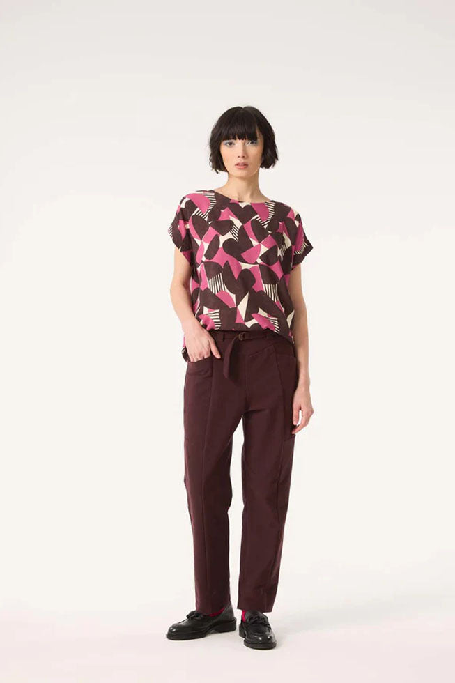 A woman wearing the Ombre Top by Cokluch in Berry Half Moon print, featuring a round neck, short dropped sleeves, and a loose fit in OEKO-TEX certified viscose, with the Belief pants in Shiraz, standing in front of a white background.