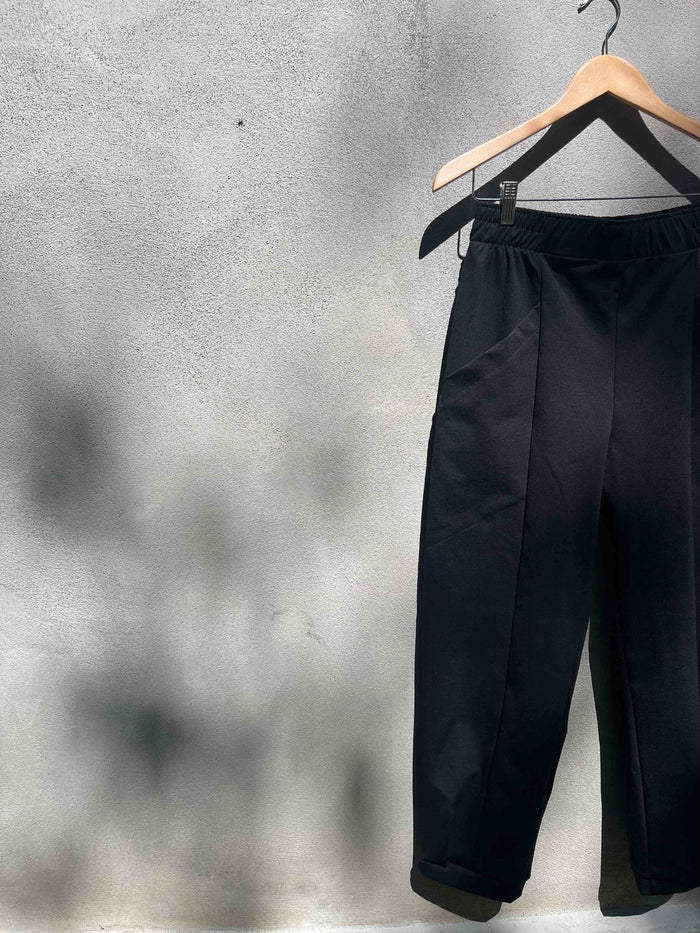 The Herbst Pant by Kazak in Black Knit, hanging against a grey wall 