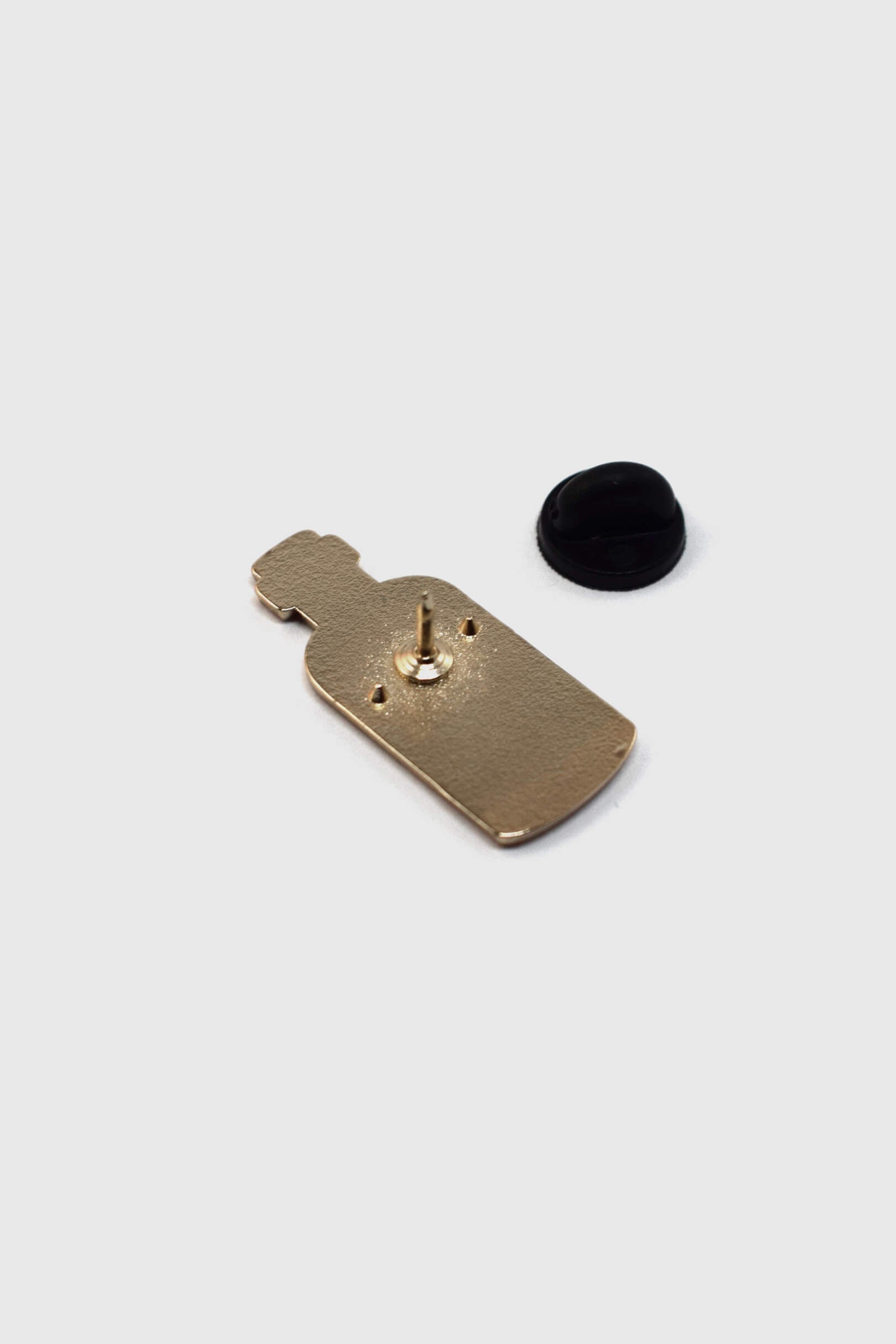A back view of the Poison Pin by Badaboöm Studio, featuring a tiny bottle of poison, is shown against a white background. 