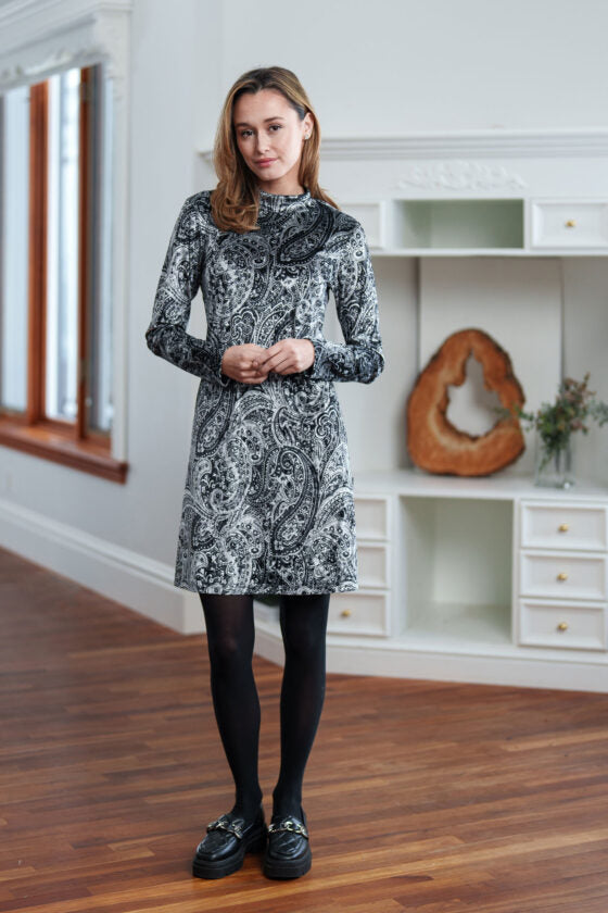 A woman wearing the Frida Dress by Rien ne Perd in Black and White Velvet stands in front of a white cabinet 