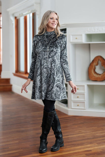 A woman wearing the Frida Dress by Rien ne Perd in Black and White Velvet stands in front of a white cabinet 