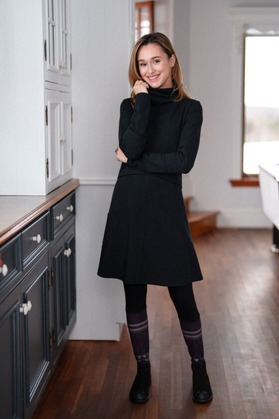 A woman wearing the Suzor Tunic-Dress by Rien ne se Perd in Black, standing by a set of cupboards