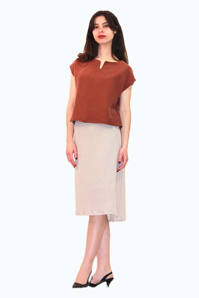 A woman wearing the Cassia Top by Ramonalisa in Sienna, a short top with short drop-shoulder sleeves, and a round neck with a v-notch at the front. She is wearing it with a beige skirt and standing in front of a white background. 