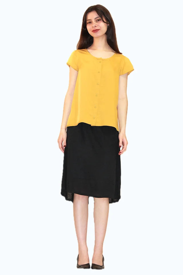 A woman wearing the Juniper Top by Ramonalisa, a button-front top with a round neck, cap sleeves, and a relaxed fit. She is wearing it with the Baobab Skirt in Black and standing in front of a white background. 