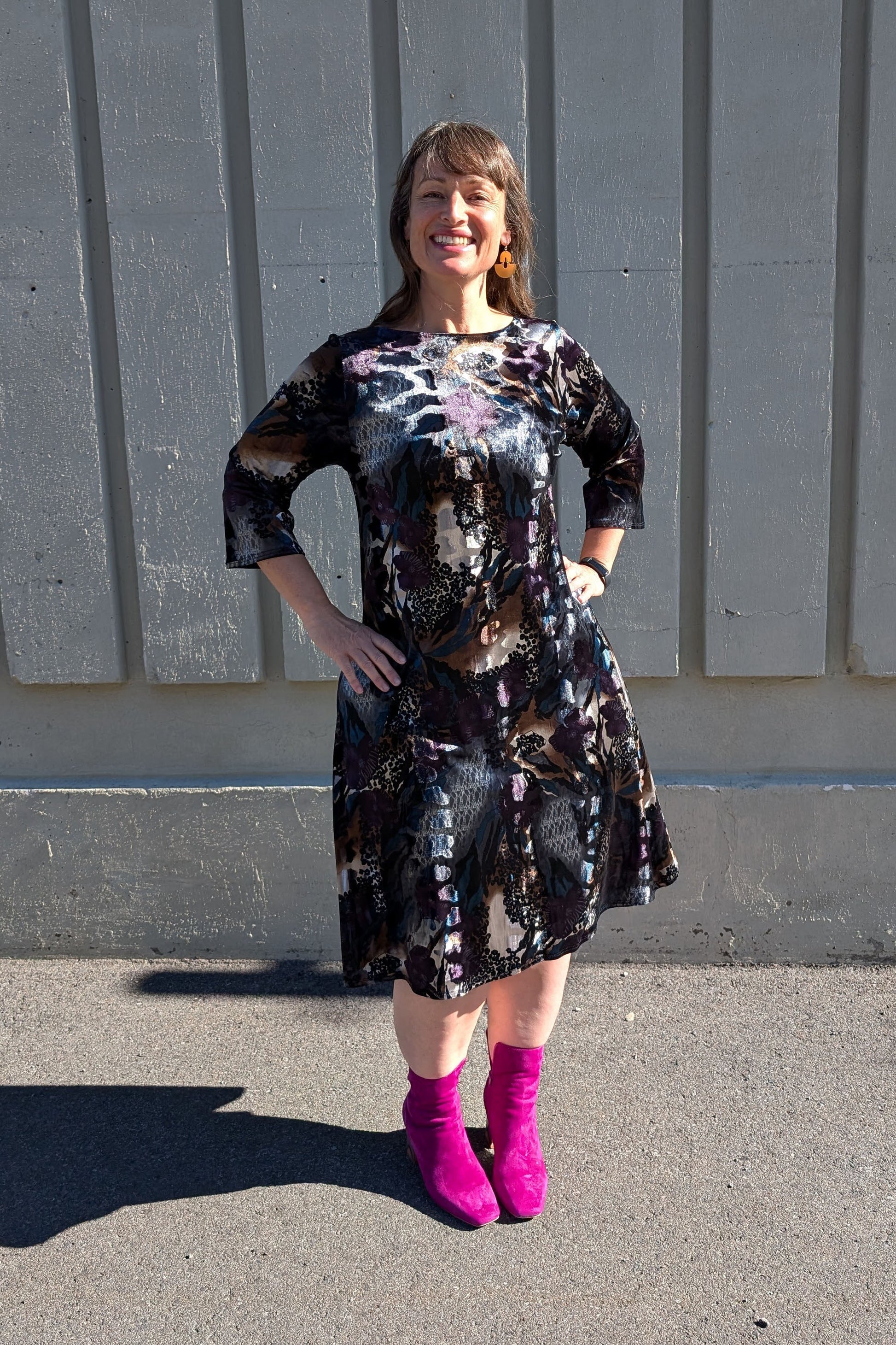 A woman wearing the Casual Dress by SI Design in Velvet Hues Blues, with a round neck, 3/4 sleeves, a loose fitting A-line shape, and a knee length, standing outside in front of a white wall. 