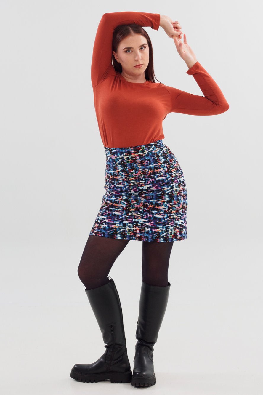 A woman wearing the Eve Skirt by Slak in a Multicolour print with an orange top, standing in front of a white background 