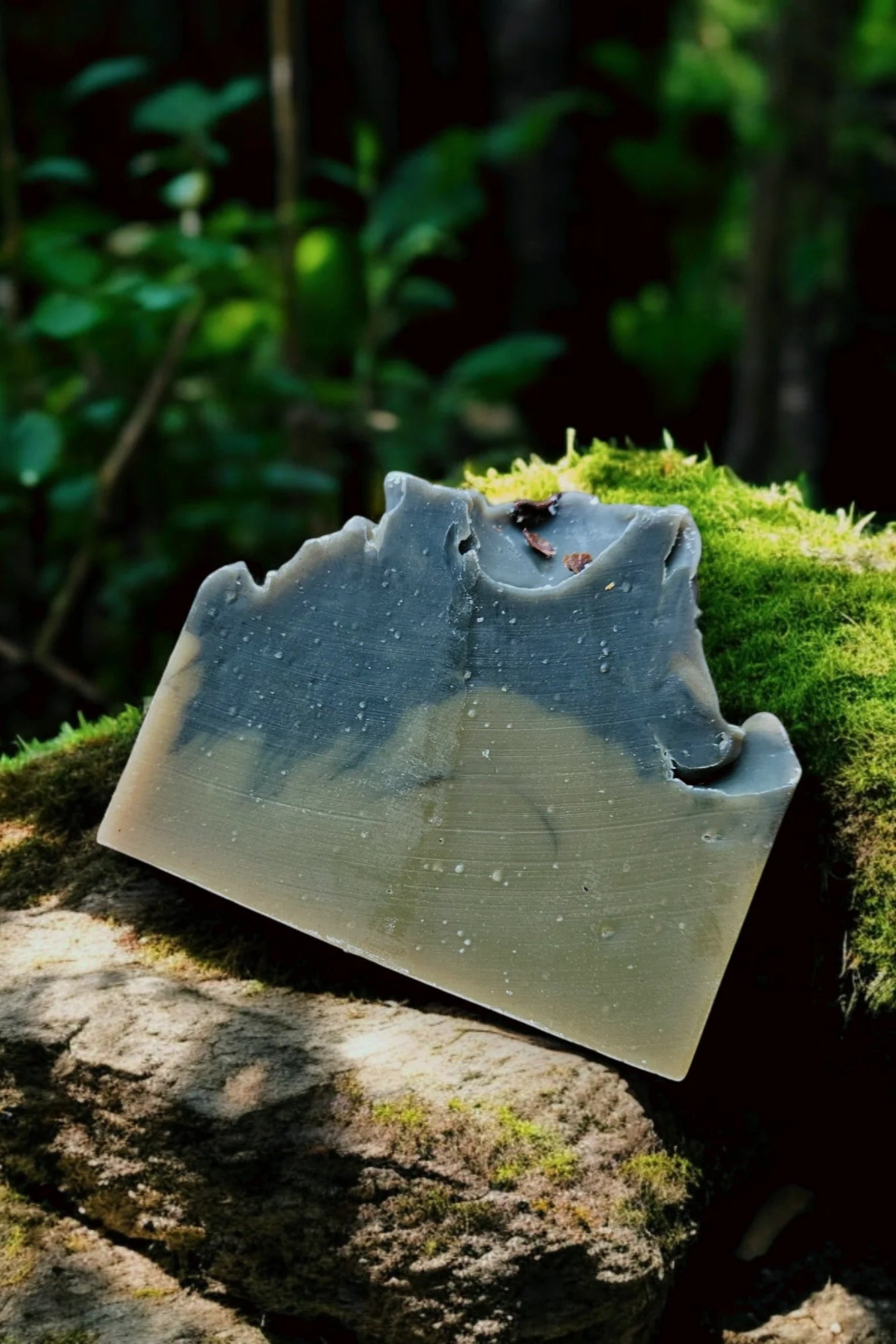 A bar of 'Dark Woods' Soap by Stay Wild Apothecary is shown on moss in a forest setting. 