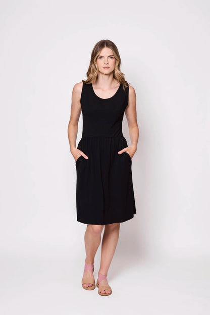 A woman wearing the Mai Dress by Tangente in Black,a  sleeveless dress with a scooped neck and gathered knee-length skirt. She is standing against a white background