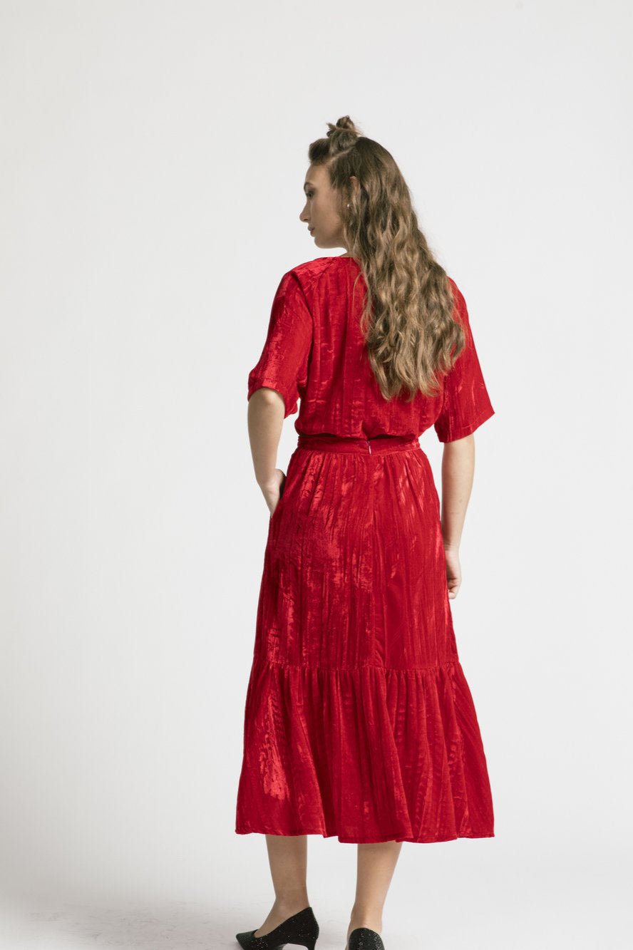 Back view of a woman wearing the Thornbirds Skirt by Allison Wonderland in red velvet, with the Wuthering Top, standing in front of a white background  