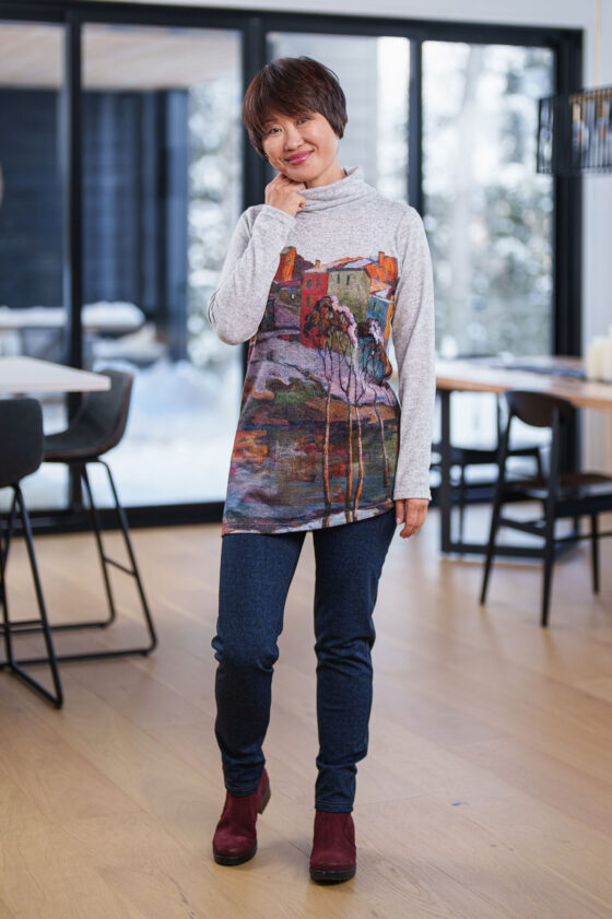 A woman wearing the Granite Pants by Rien ne se Perd in Denim Blue, standing by tables and chairs in front of a large window