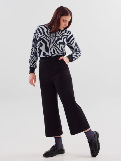 A woman wearing the Wanda Sweater in Blue Zebra print by Slak with black pants, standing in front of a white background 