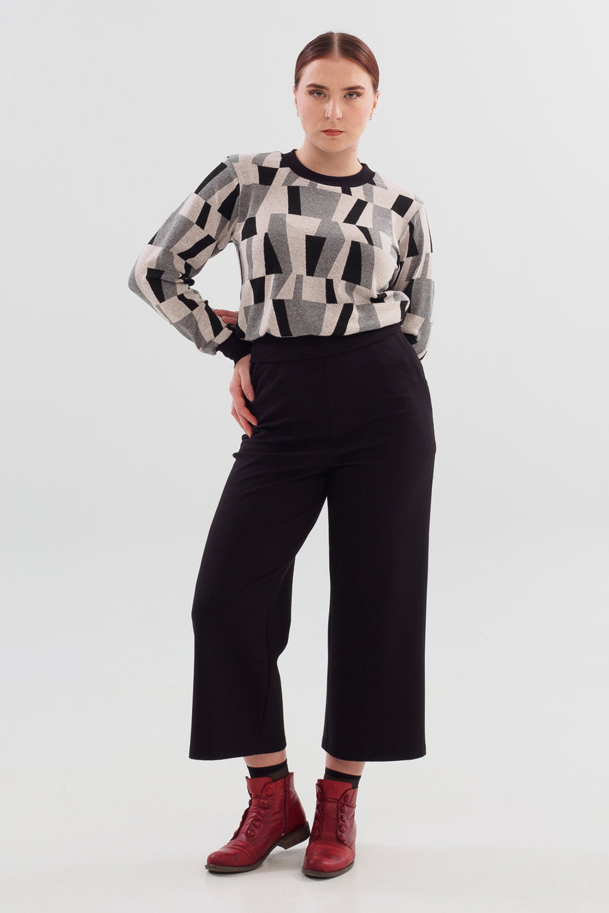 A woman wearing the Wanda Sweater in Black with Grey print by Slak with black pants, standing in front of a white background 