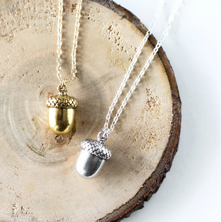 Tiny acorn necklace by Birch Jewellery, in silver and gold, styled on a stump of wood