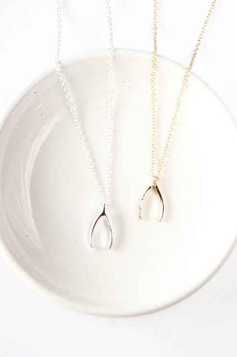 Wishbone necklace by Birch Jewellery; silver and gold plated brass; styled on a white ceramic dish; overhead view