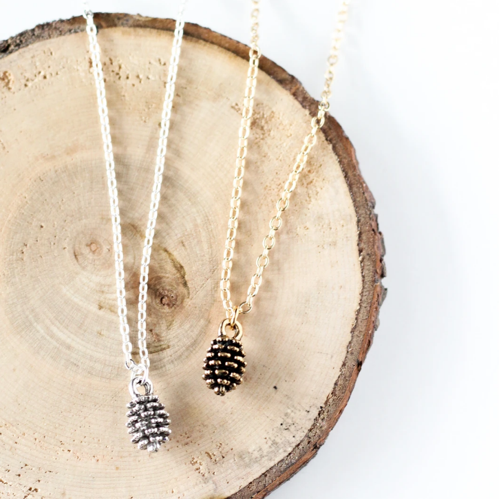 Tiny pine cone necklace by Birch Jewellery in silver and gold, styled on a stump of wood