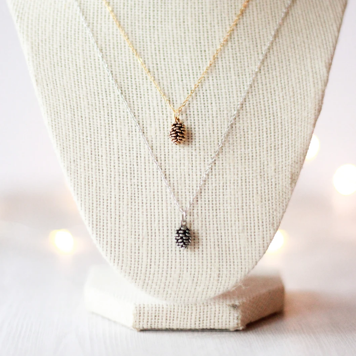 Tiny pine cone necklace by Birch Jewellery in silver and gold, styled on a jewellery display