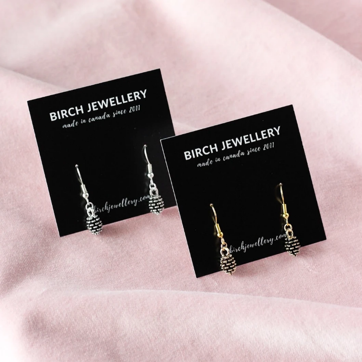 Birch Jewellery Made in Canada since 2011; pine cone earrings in silver and gold; in packaging; styled on a blush cloth