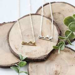 Mountain necklace by Birch Jewellery; silver and gold; flat lay styled on a a pile of wooden stumps and eucalyptus