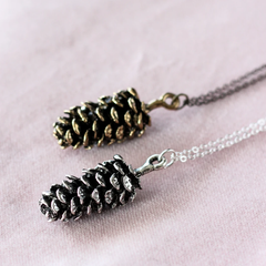 Large pine cone necklace by Birch Jewellery; flat lay; in silver and gold; styled on a blush cloth