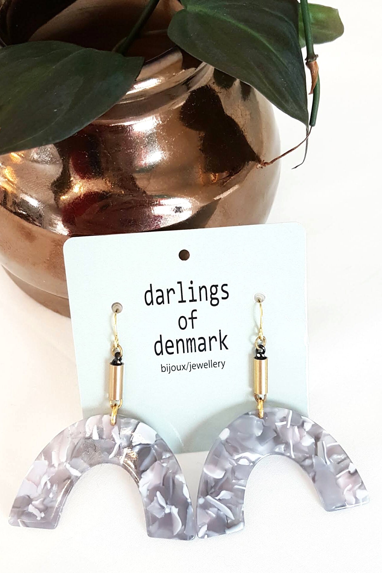 Vuttue dangle earring by Darlings of Denmark; grey pearlescent textured acrylic arch shapes hanging off raw brass tubes; flay lay with packaging