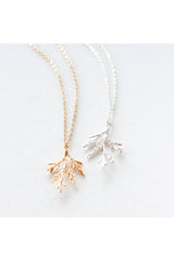 Juniper branch necklace by Birch Jewellery; shown in silver and hold; flat lay on a white surface