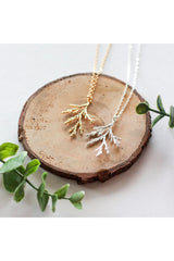 Juniper branch necklace by Birch Jewellery; shown in silver and hold; flat lay on a stump of would and with eucalyptus branches