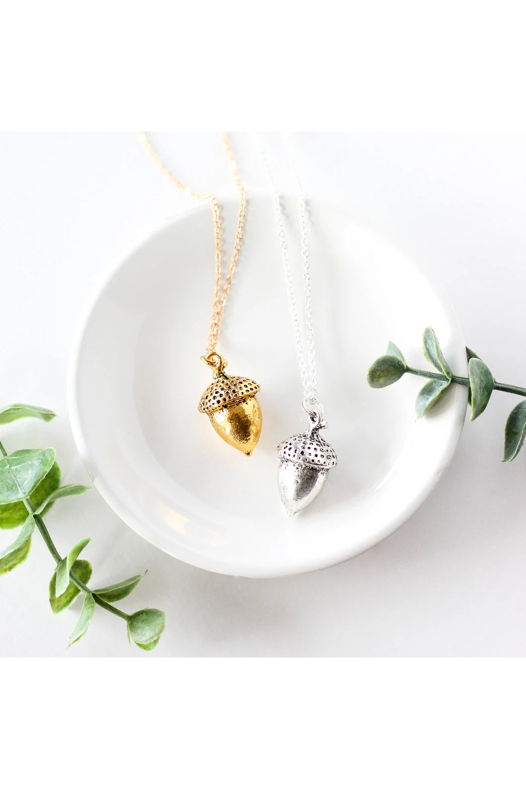 Large acorn necklace by Birch Jewellery; shown in silver and gold; flat lay; styling on a white ceramic dish and with eucalyptus branches