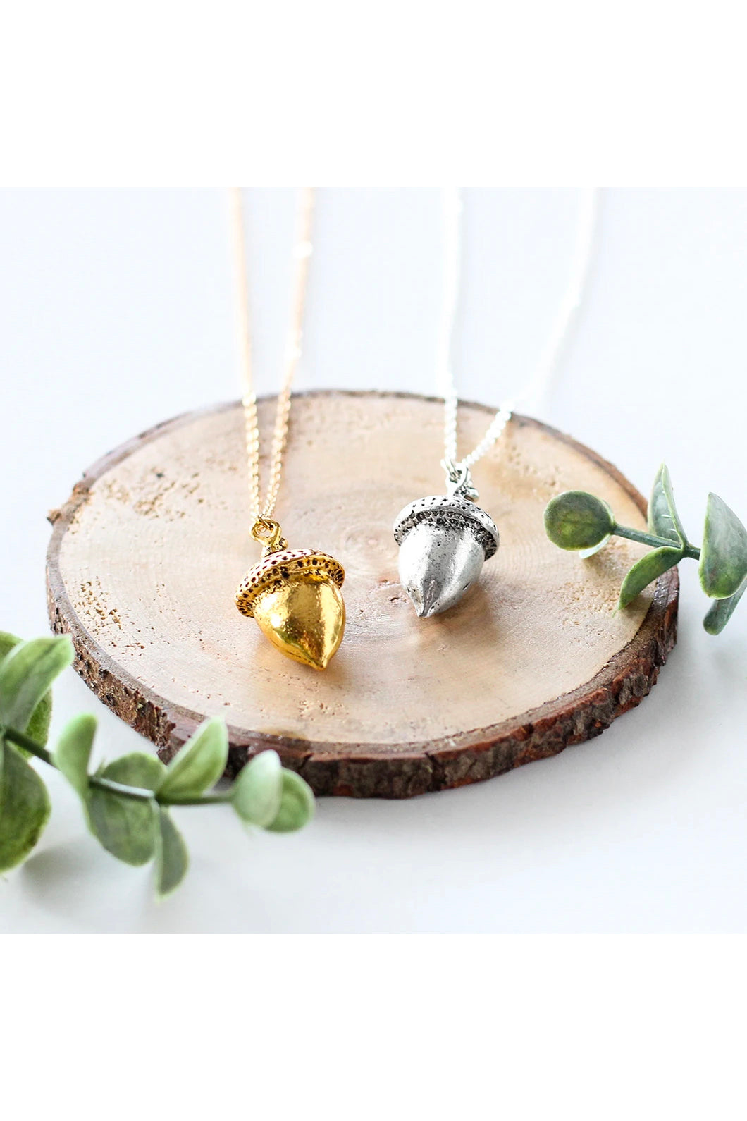 Large acorn necklace by Birch Jewellery; shown in silver and gold; flat lay; styling on a stump of wood and with eucalyptus branches