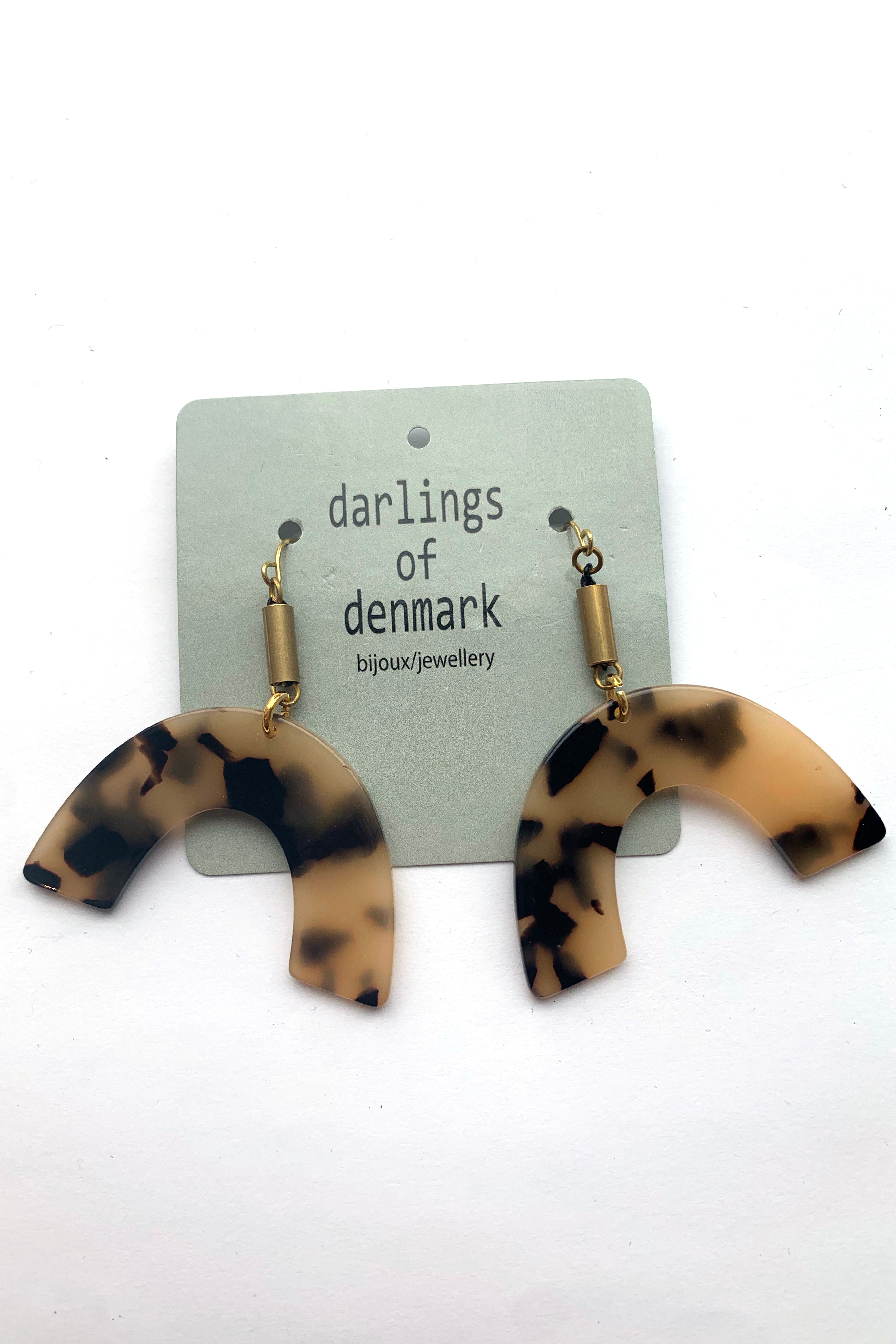 Vuttue dangle earring by Darlings of Denmark; light tortoise shell acrylic arch hanging off raw brass tubes; flat lay