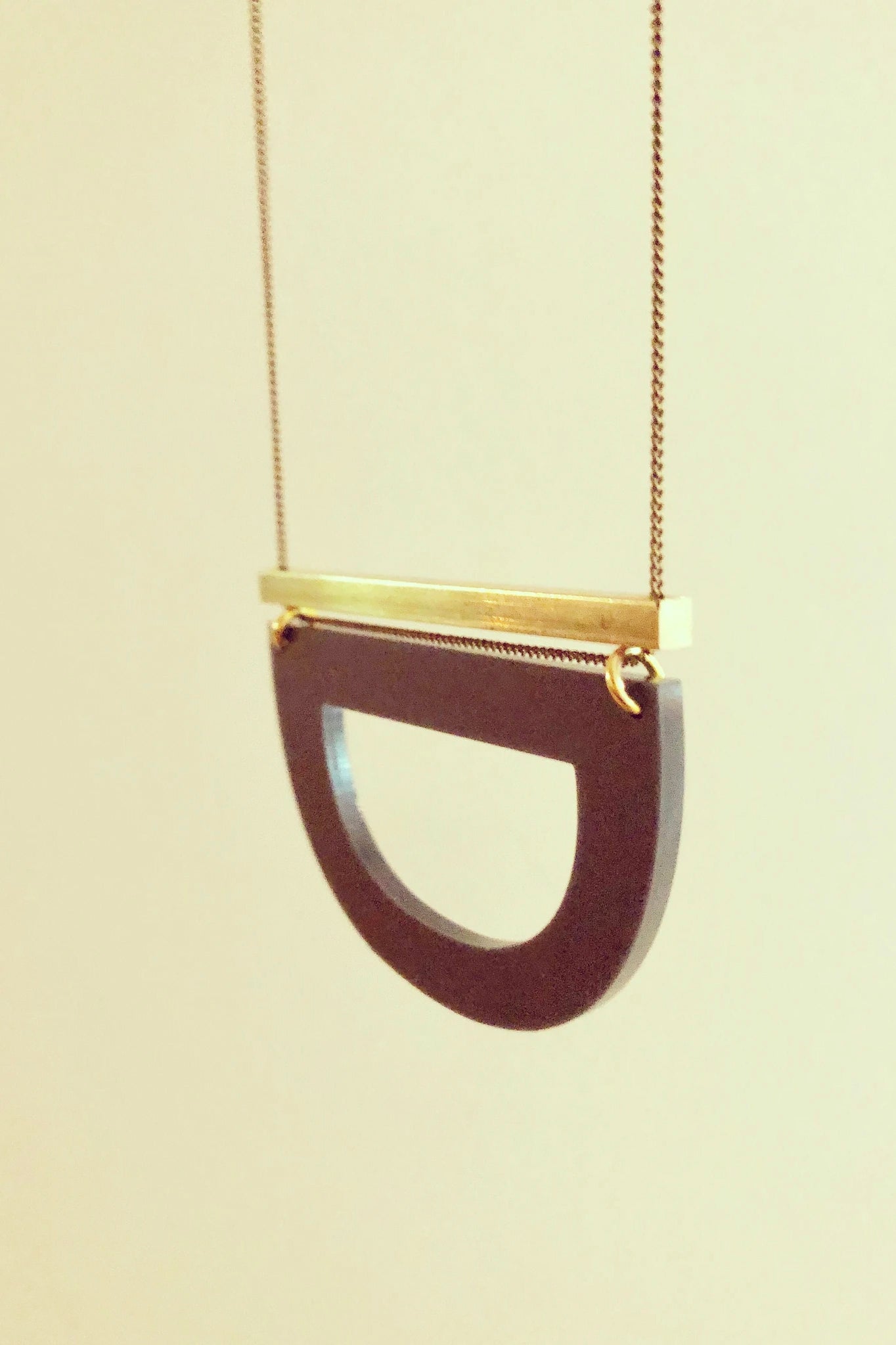 Luppe long necklace by Darlings of Denmark; solid brass horizontal bar and acrylic hollowed out half circle; hanging flat lay